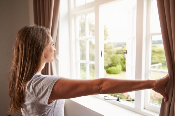 a woman standing by the bedroom window opening the curtains