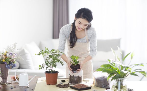 an asian woman transfering a plant to a flower glass inside the living room