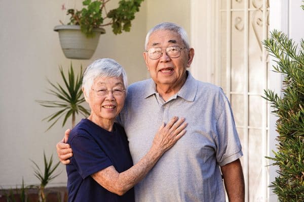 a happy elderly couple standing in front of their house