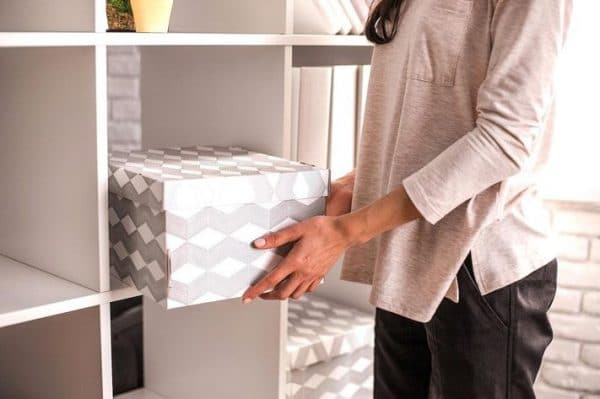 a woman placing a grey cardboard box on the shelf