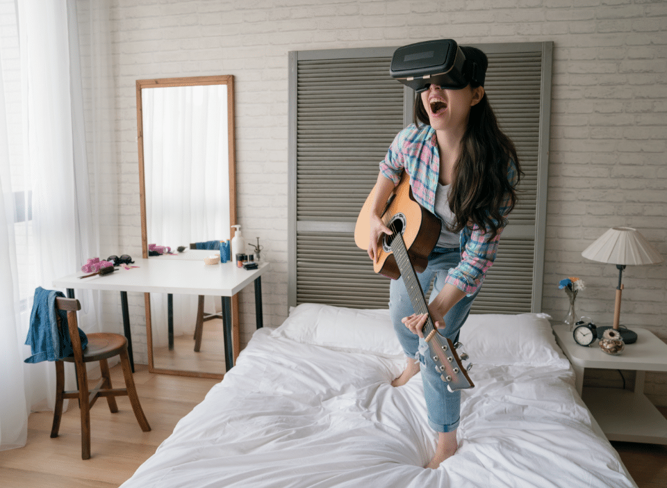 Rectangle 107 A woman standing on her bed while holding a guitar while looking into VR