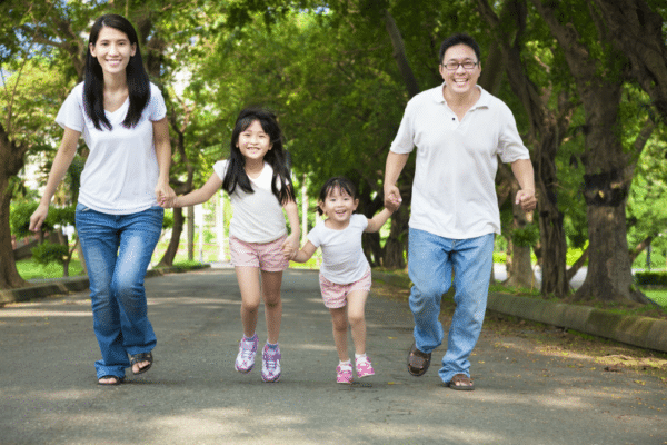 An Asian family happily holding hands while walking through the park