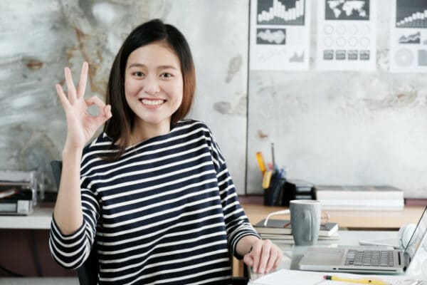 an asian woman doing the okay sign while working in her office