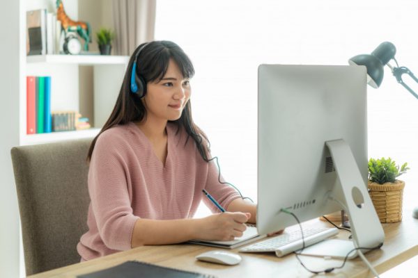 an asian woman wearing a headset while listening to her online class